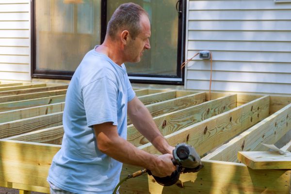 Installing of wooden deck patio carpenter hammering on a deck patio